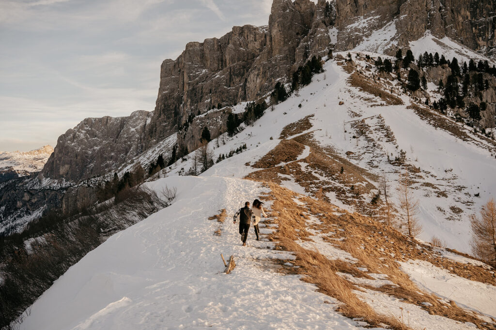 Couple hiking snowy mountain trail at sunset