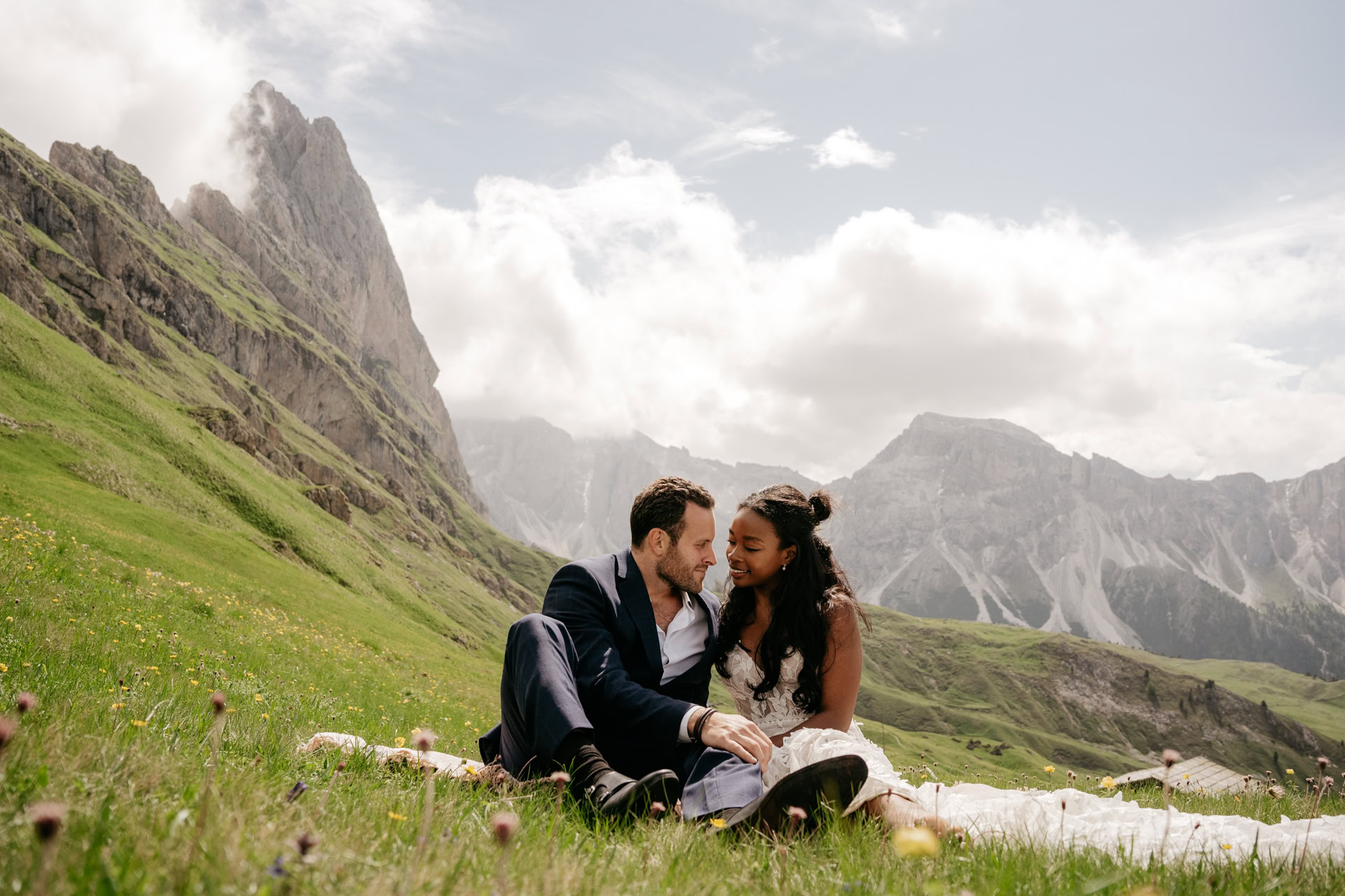 Couple sitting on mountainside meadow, smiling, lovely scenery.