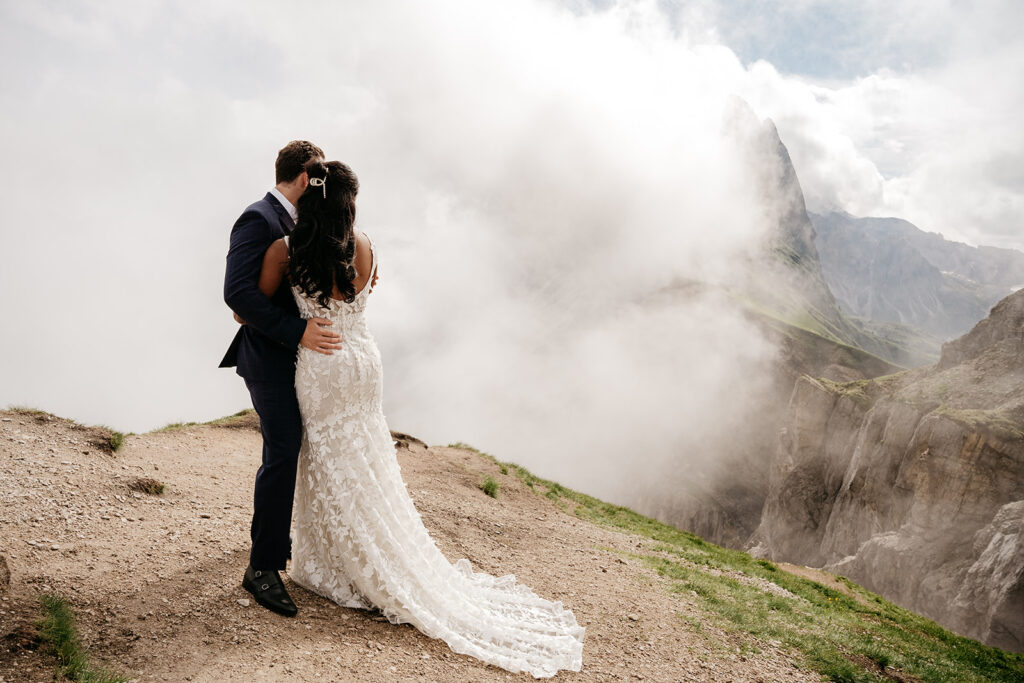 Bride and groom on mountain edge with clouds.