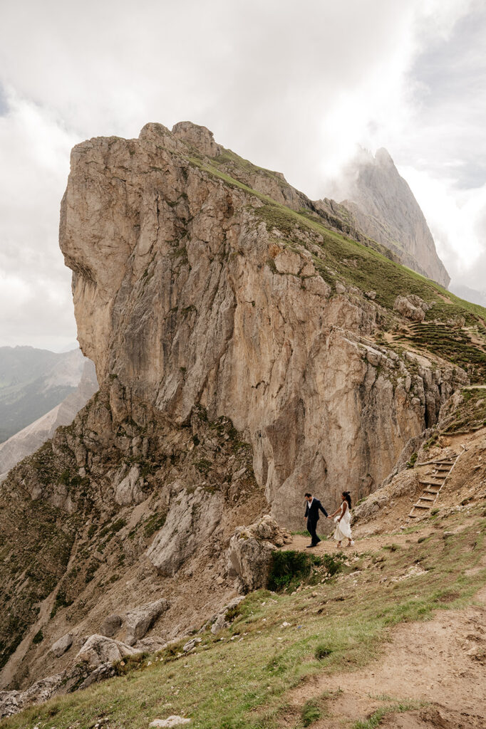 Bride and groom walking on mountainous trail.