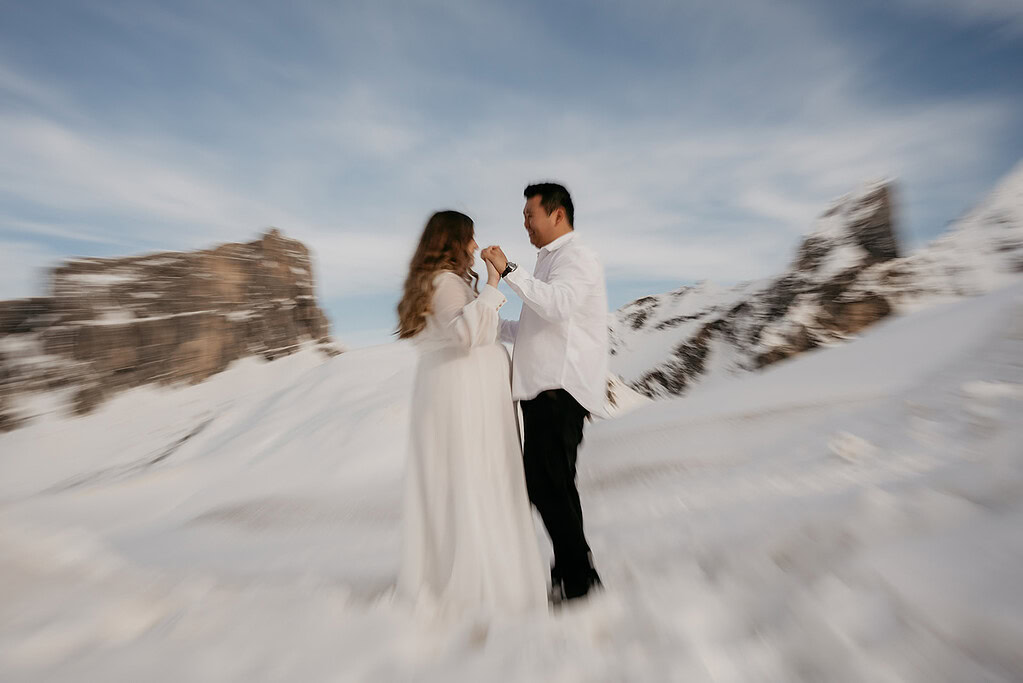 Couple in white clothing on snowy mountain landscape.