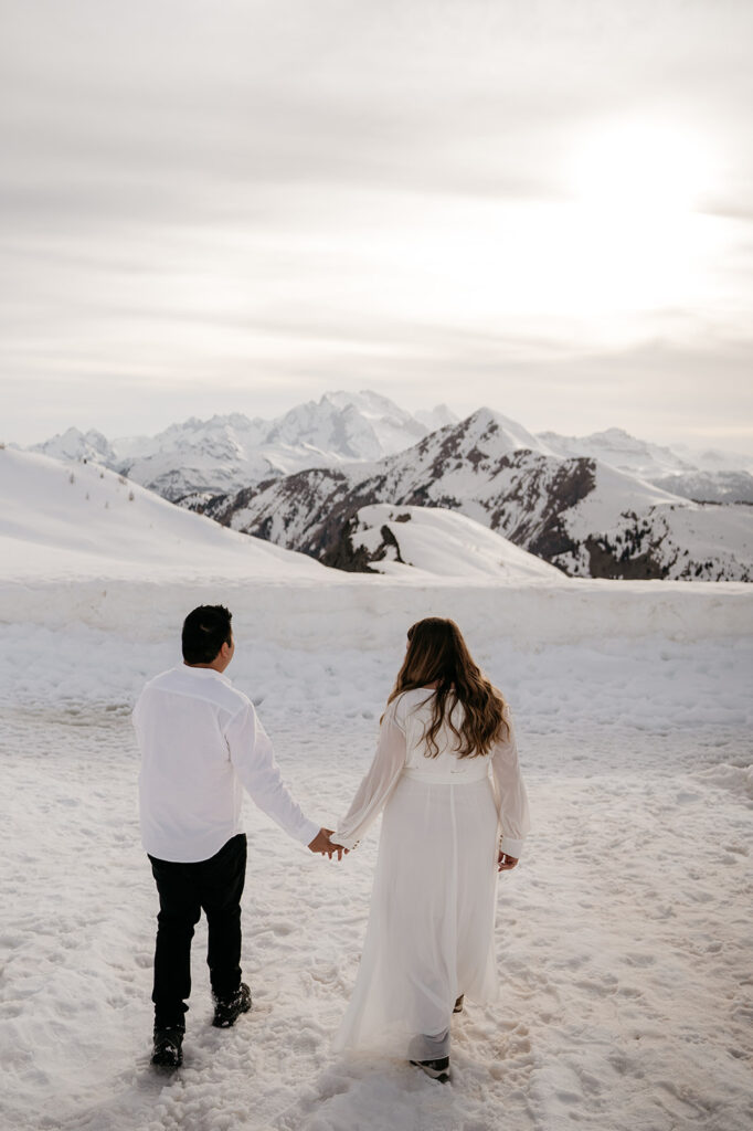 Couple holding hands on snowy mountain summit.