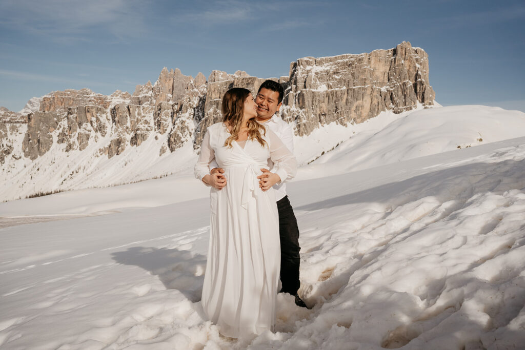 Couple embraces on snowy mountain landscape.