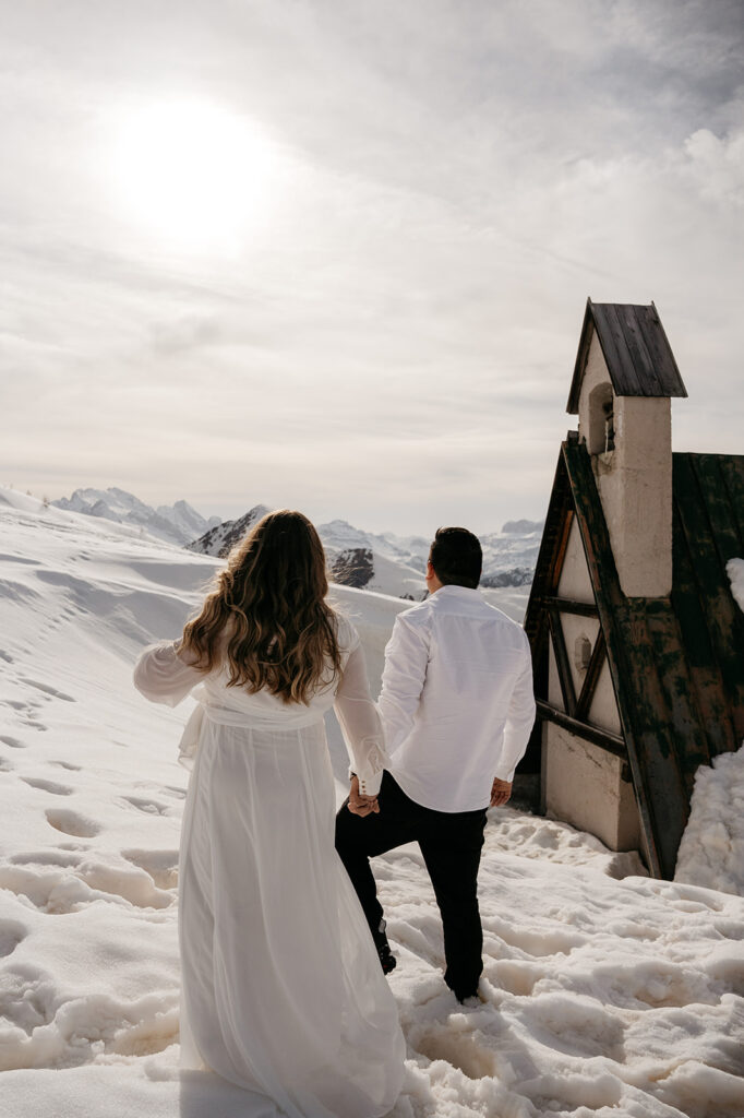 Couple holding hands on snowy mountain path.