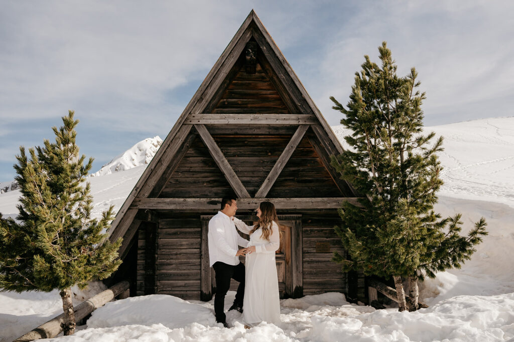 Couple outside A-frame cabin in snowy mountains.