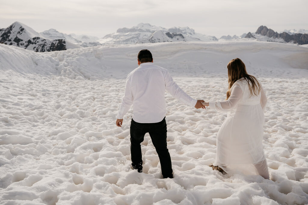 Couple holding hands, walking on snowy mountains.