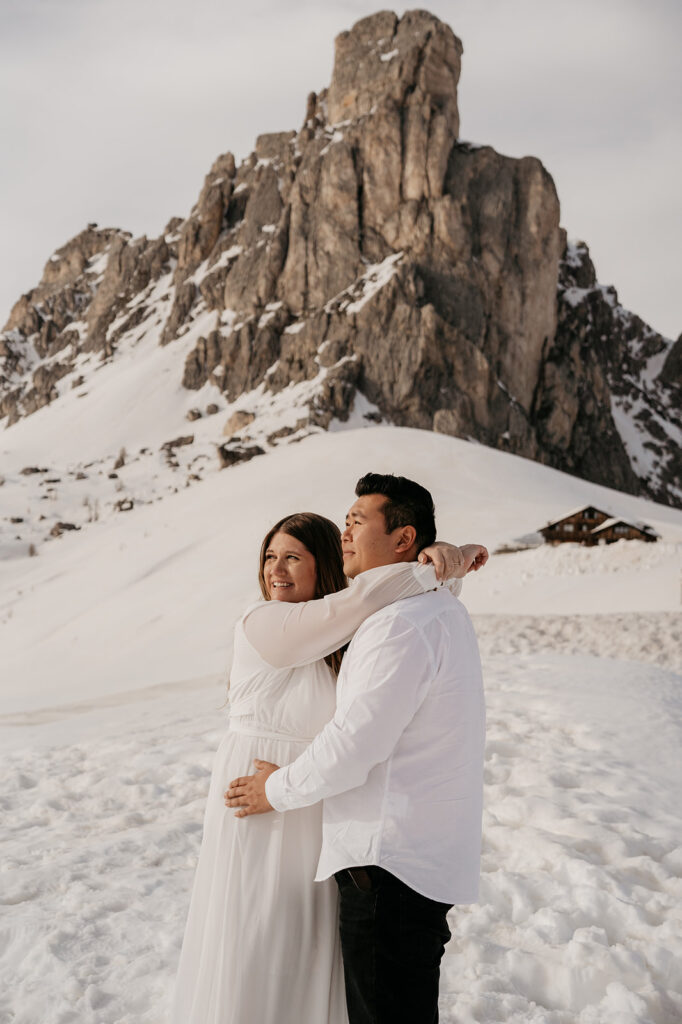 Couple embraces on snowy mountain landscape.