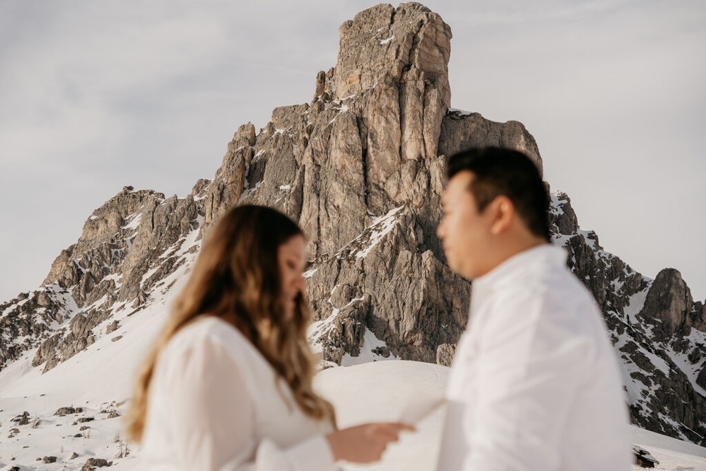 Couple stands in snowy mountain landscape.