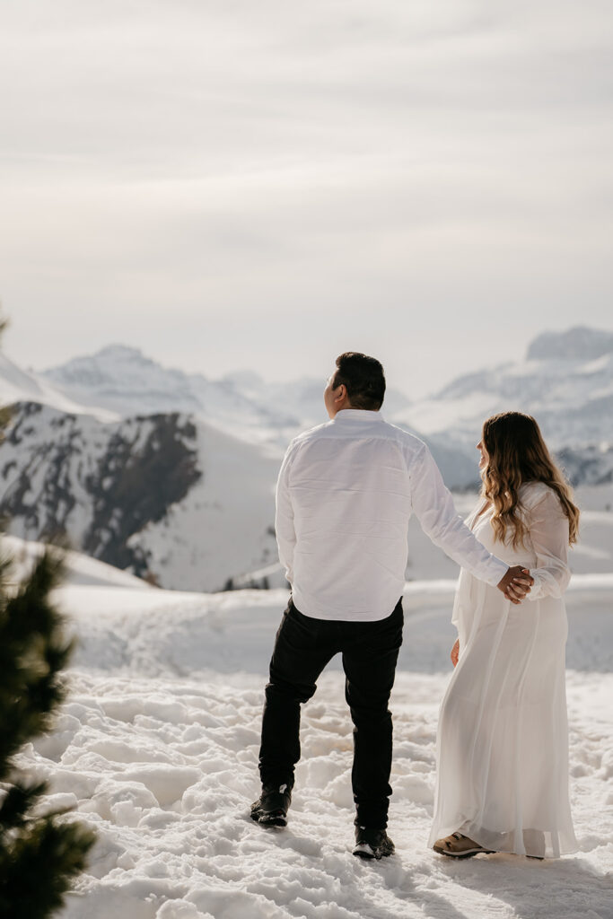 Couple holds hands, snowy mountain landscape.