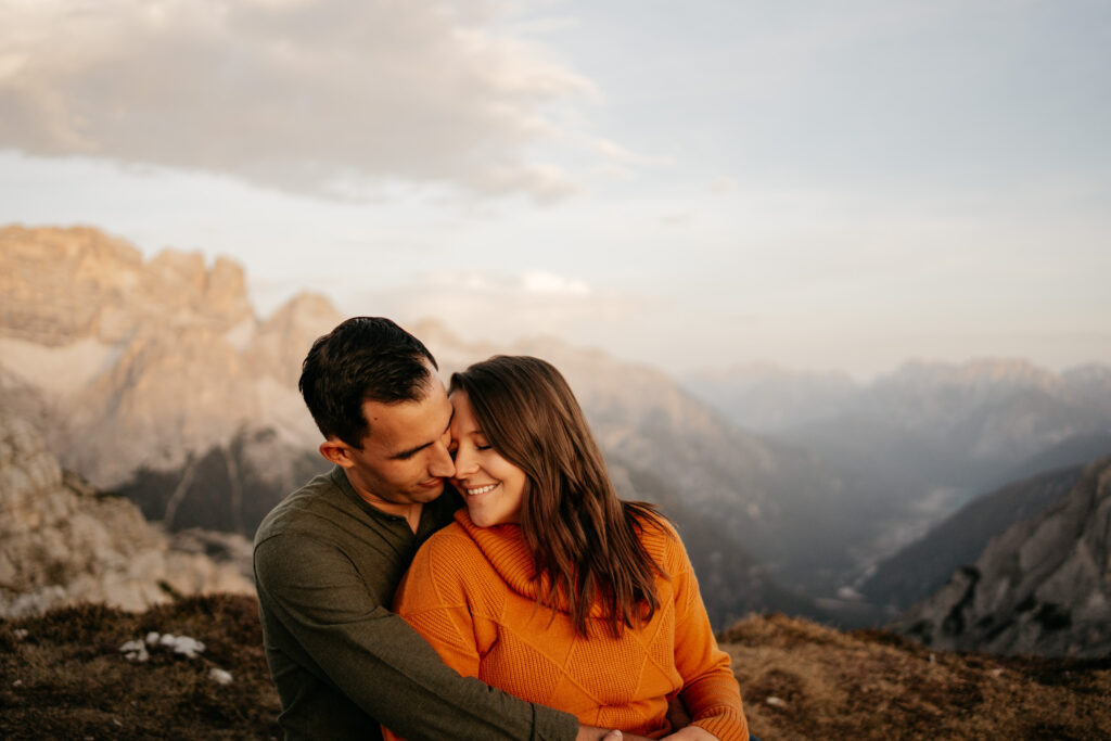 Couple embraces with mountains in background.