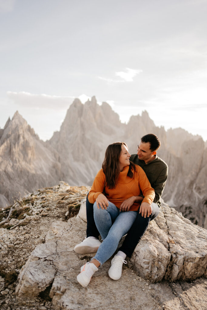 Couple sitting on mountain, smiling at each other.