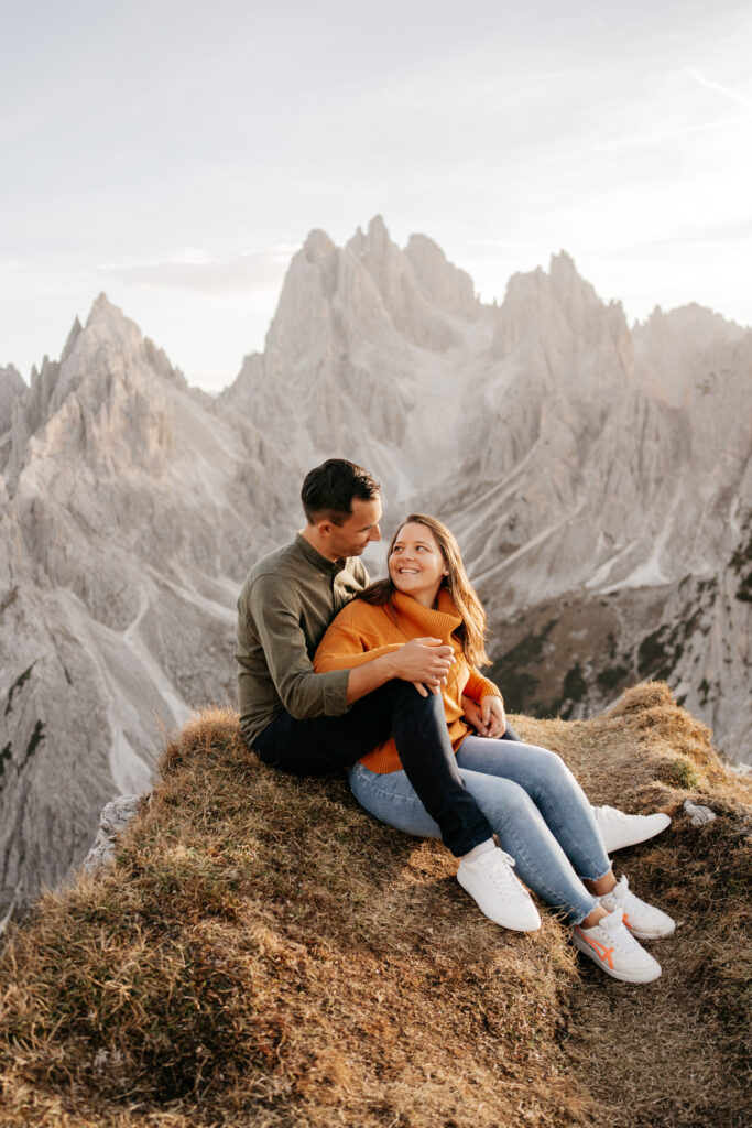 Couple sitting on mountain edge smiling.