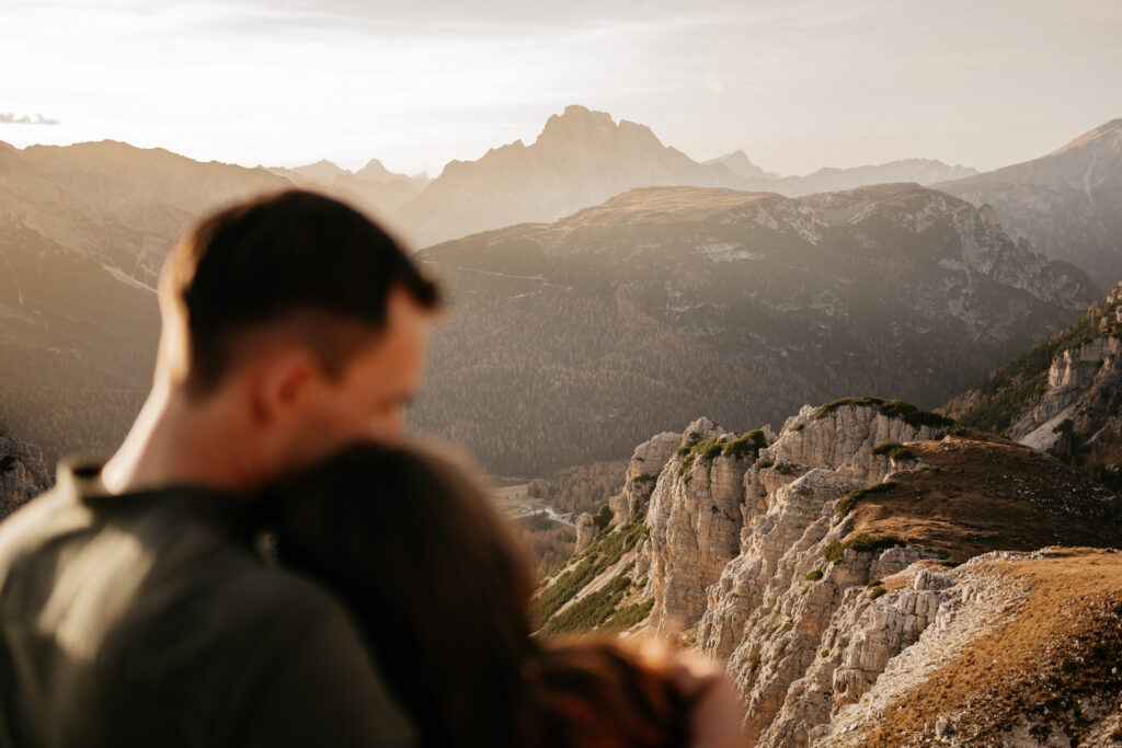 Couple embraces with mountain landscape in background.