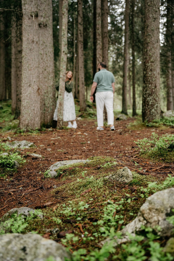 Couple walking in forest among tall trees.