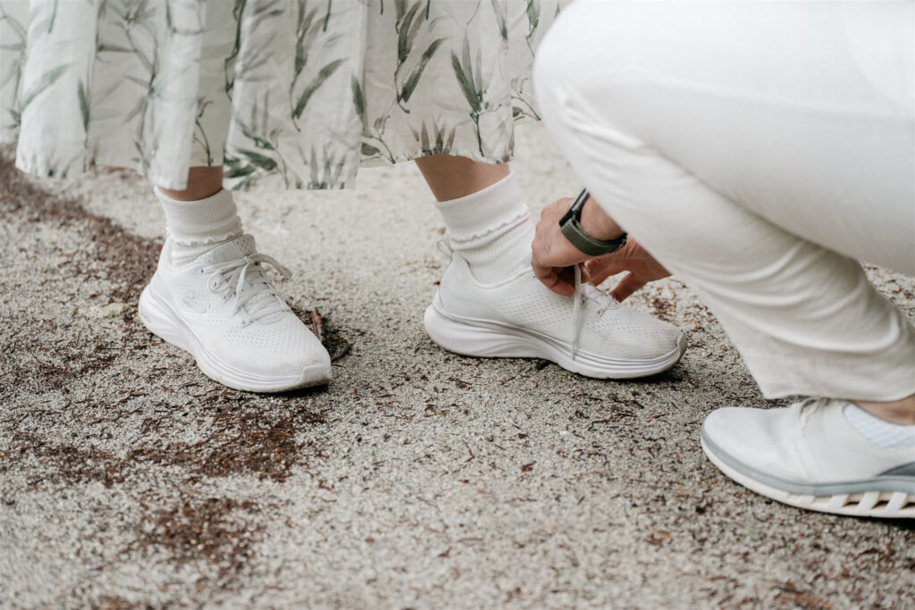 Person tying white sneakers on another's feet.