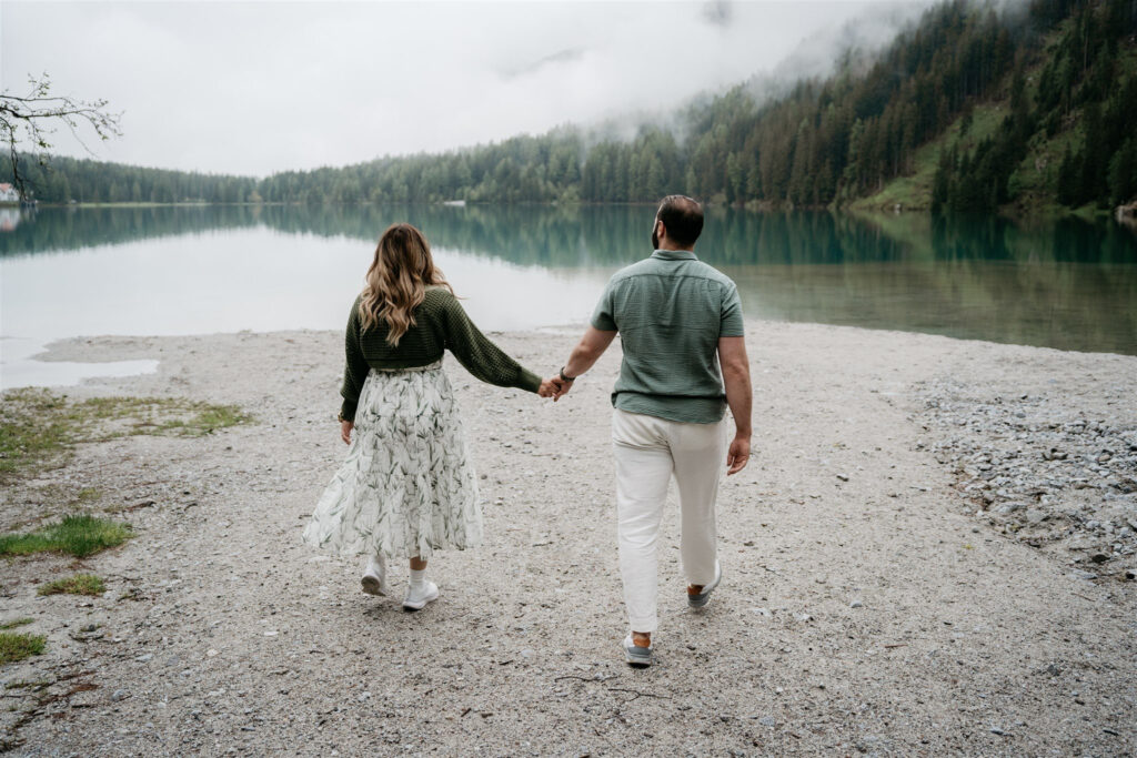 Couple holds hands walking by lake.