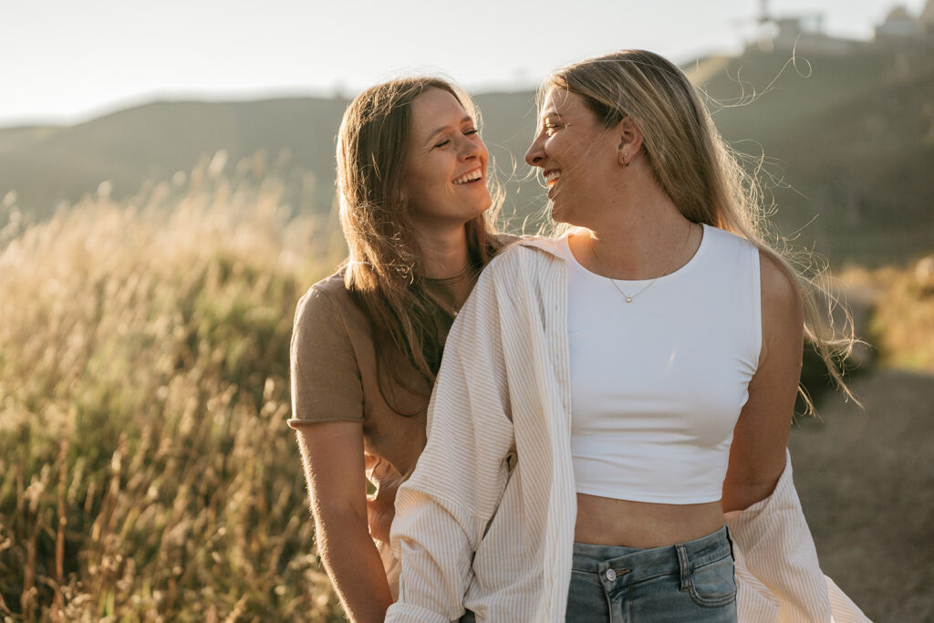 Two women smiling outdoors in a sunny field.