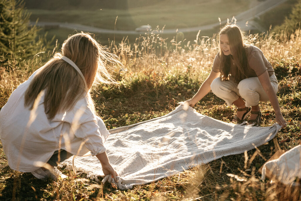 Two women spreading a blanket on grassy field.