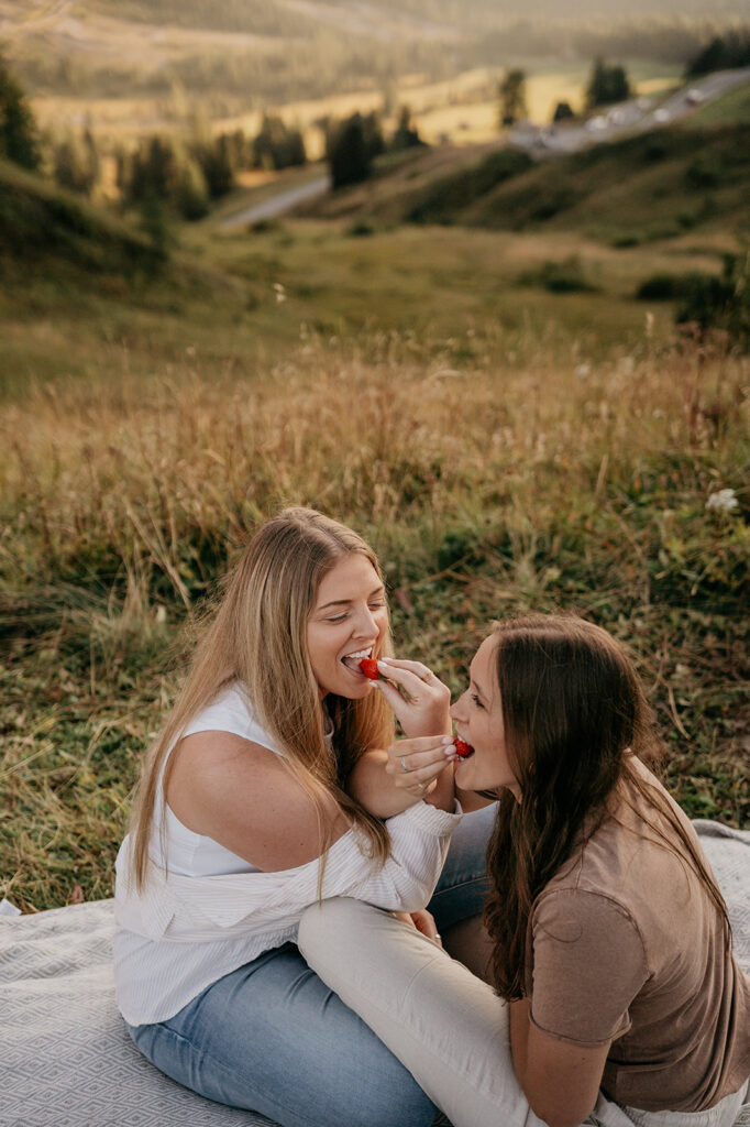 Two friends sharing strawberries outdoors, smiling together.