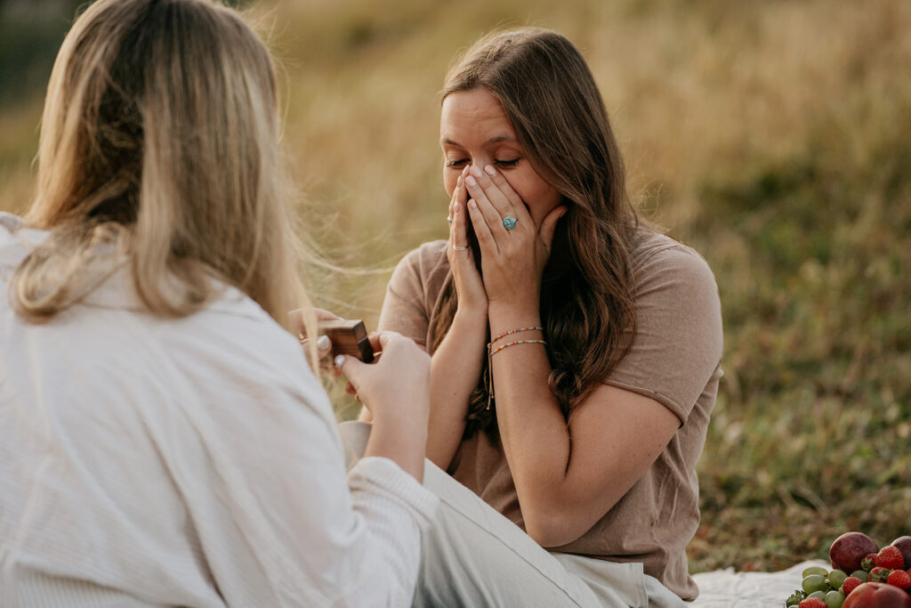 Surprised woman during outdoor proposal on picnic blanket.