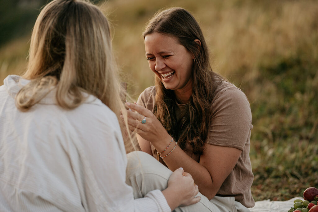 Two women laughing on a picnic blanket.