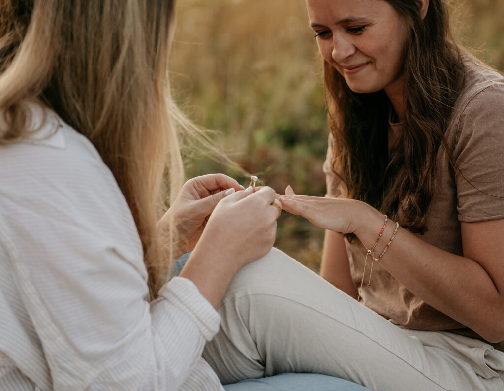 Woman placing ring on another woman's finger outdoors.