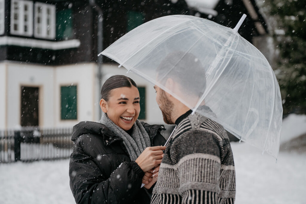 Couple smiling under transparent umbrella in snow