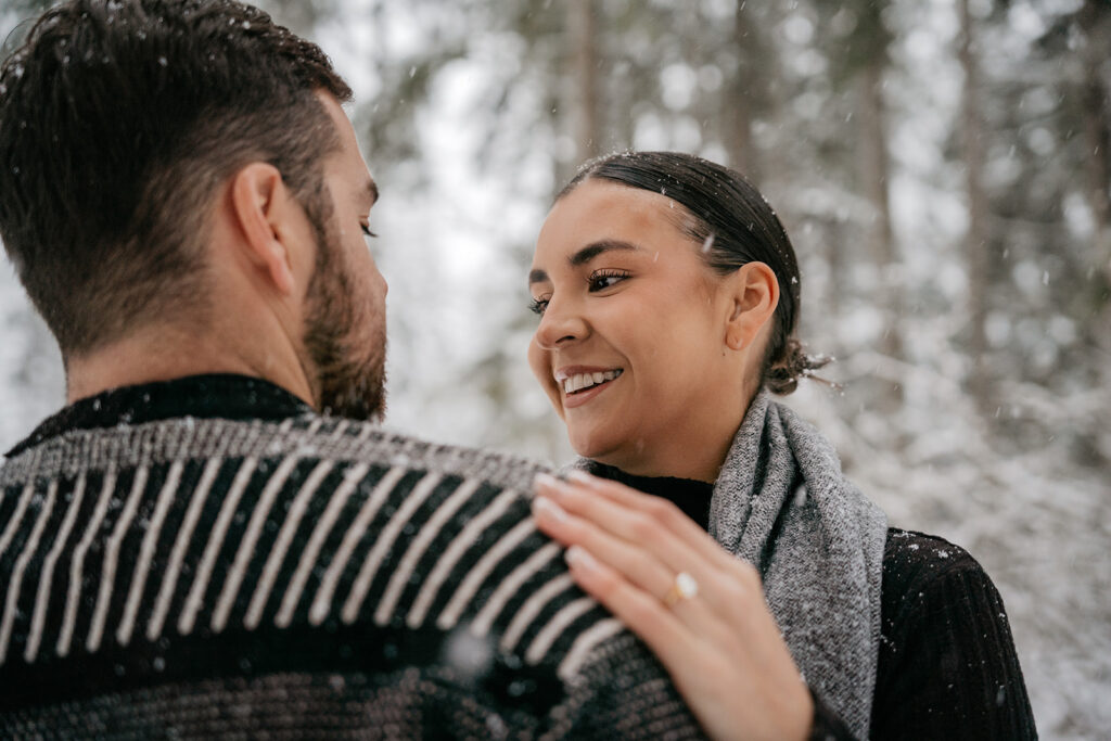 Couple smiling at each other in snowy forest.