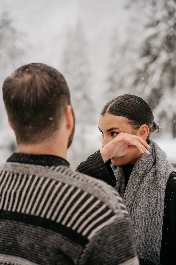 Couple in snowy forest, woman wipes tear