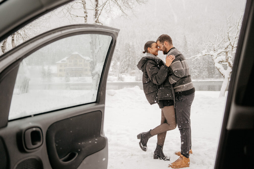 Couple embracing in snowy landscape by car door.