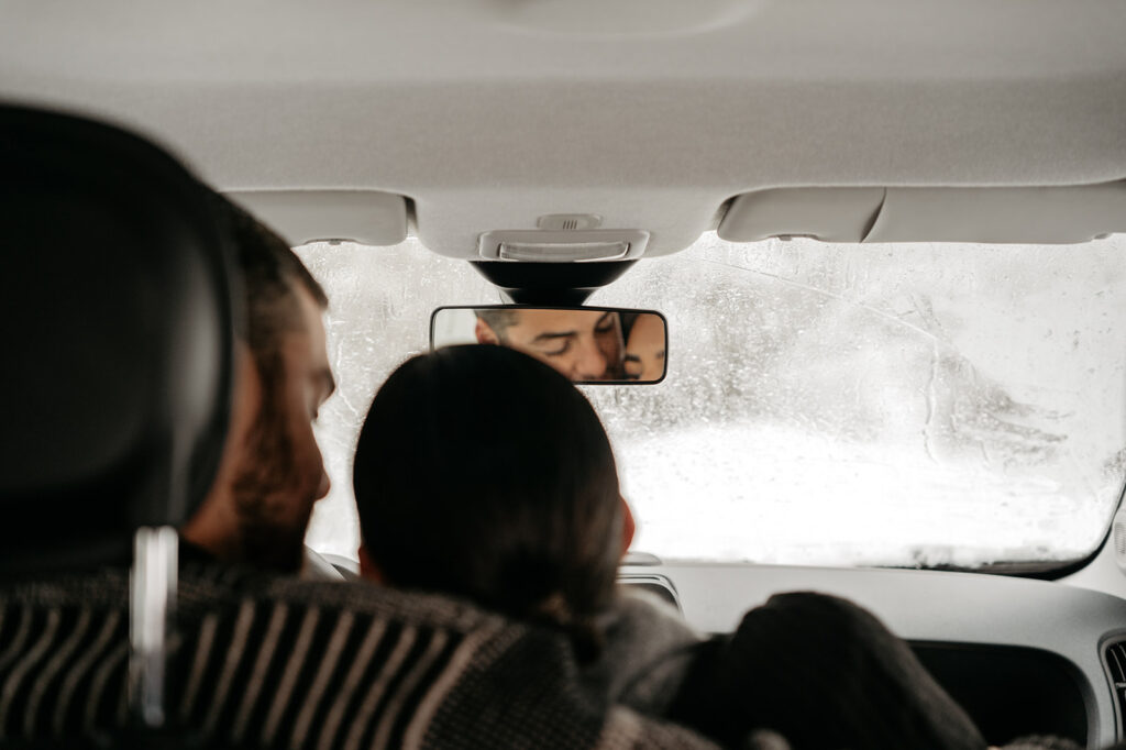 Couple in car rear-view mirror reflection, snowy window