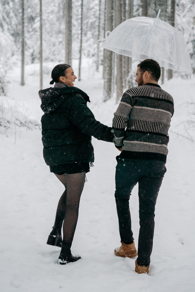 Couple walking in snowy forest with umbrella.