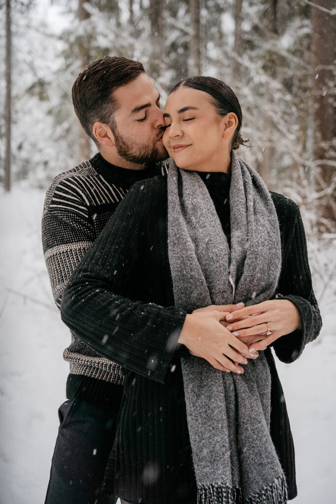 Couple embracing in snowy winter forest scene.