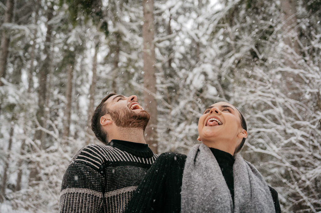 Couple catching snowflakes on tongues in snowy forest.