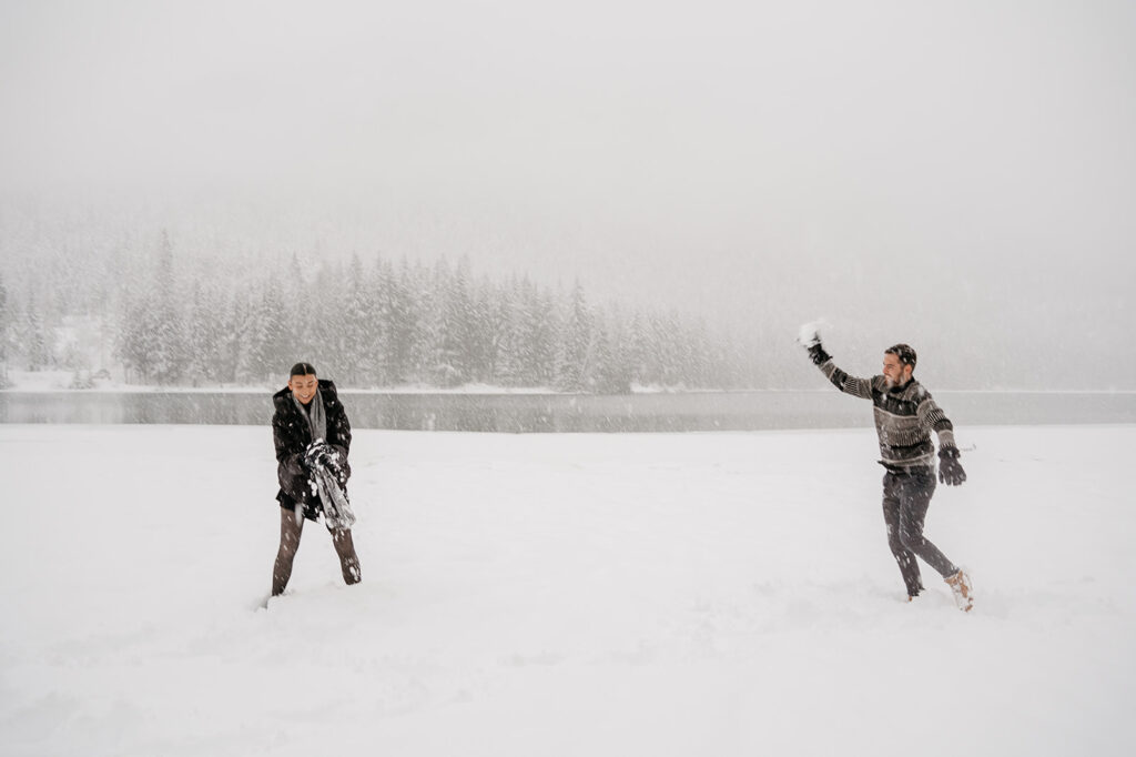 Couple playing in snowy landscape by a lake.