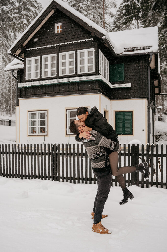 Couple kissing outside snowy cabin