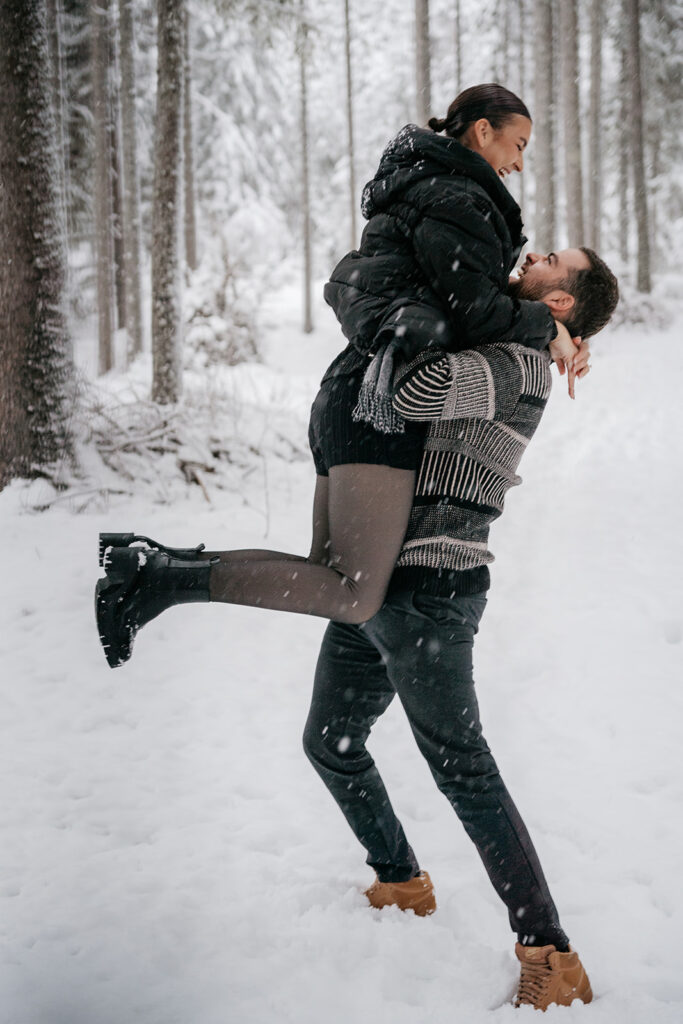 Couple joyfully embracing in snowy forest.