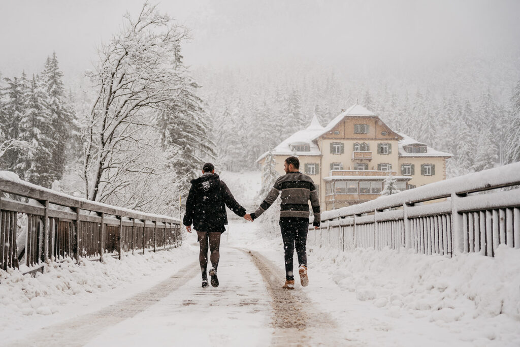 Couple walking on snowy bridge towards house.