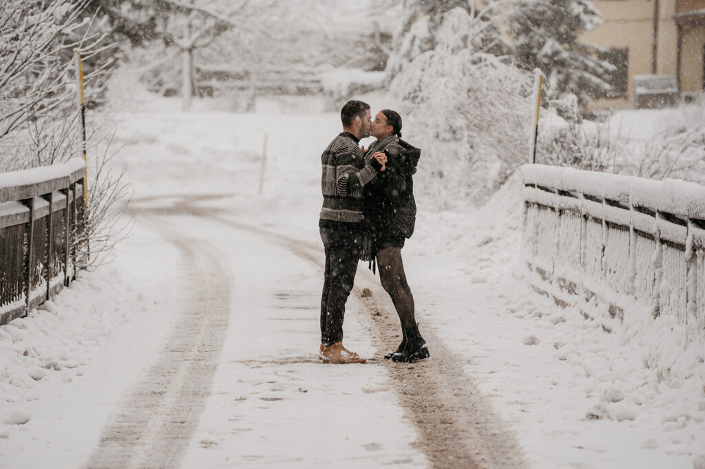 Couple standing in snowy winter landscape kissing.