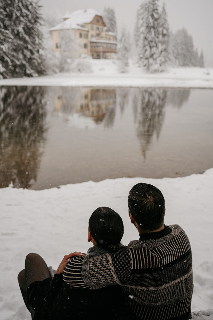 Couple embraces by snowy lake and winter cabin