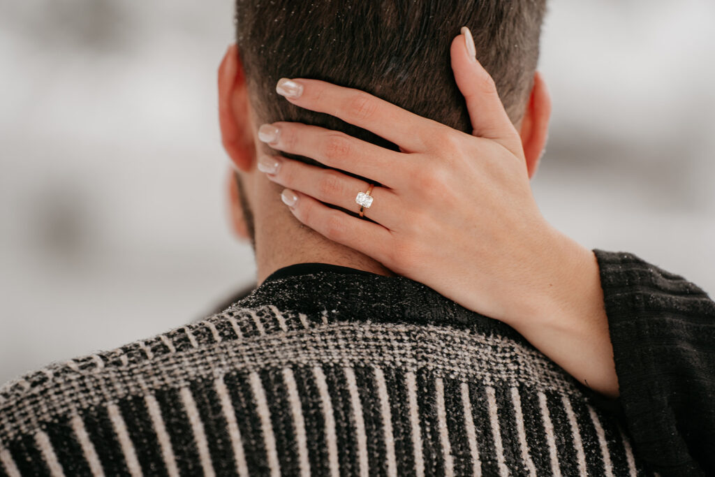 Woman's hand on man's neck, wearing engagement ring.