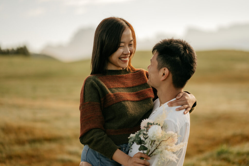 Couple embracing in scenic field, holding flowers.