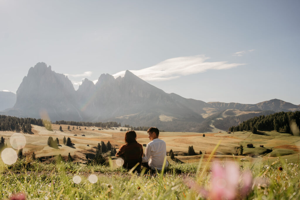 Couple sitting in field, mountain view behind.