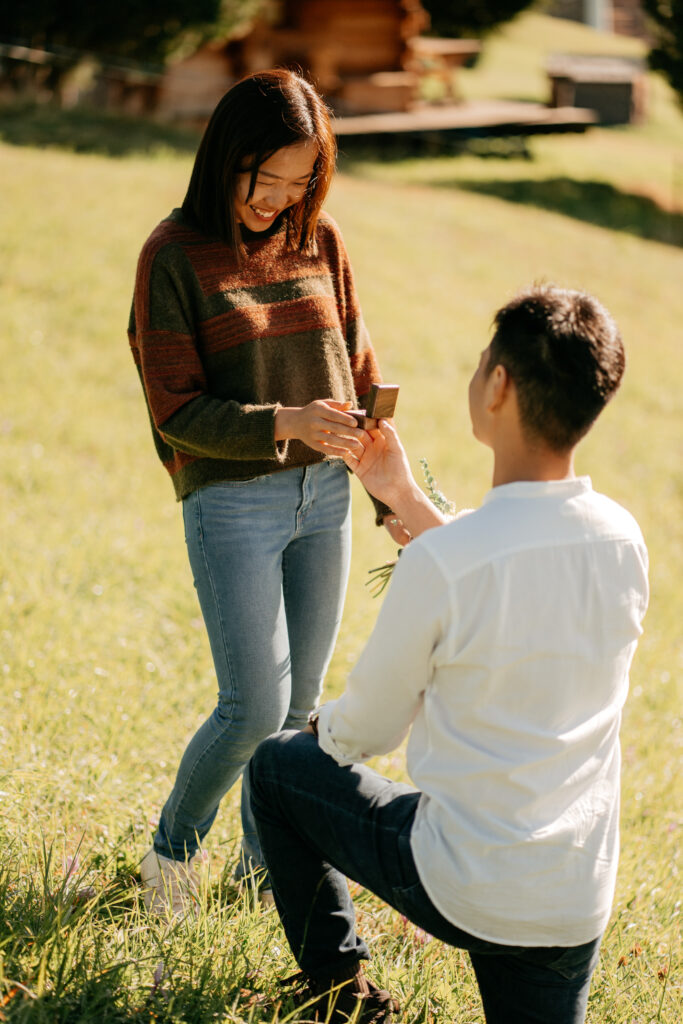 Man proposing with ring outdoors in sunny field.