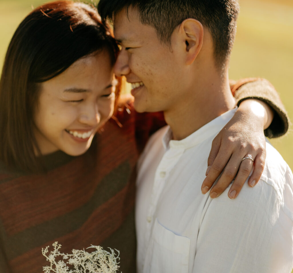 Smiling couple embracing outdoors with engagement ring.