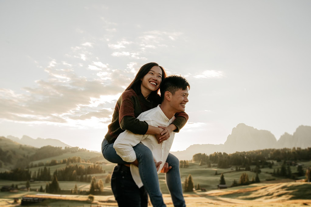 Smiling couple piggyback in scenic landscape background.