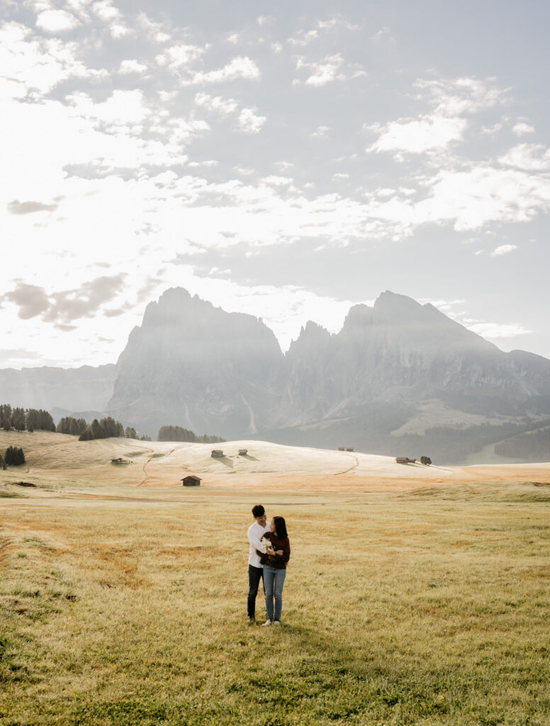 Couple embraces in scenic mountainous meadow landscape.