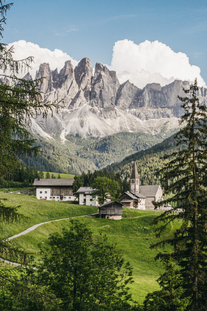 Alpine village with church, mountains in background.