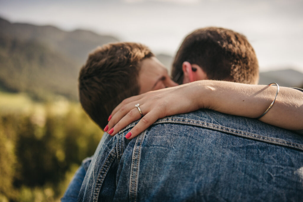 Couple embracing with engagement ring visible.