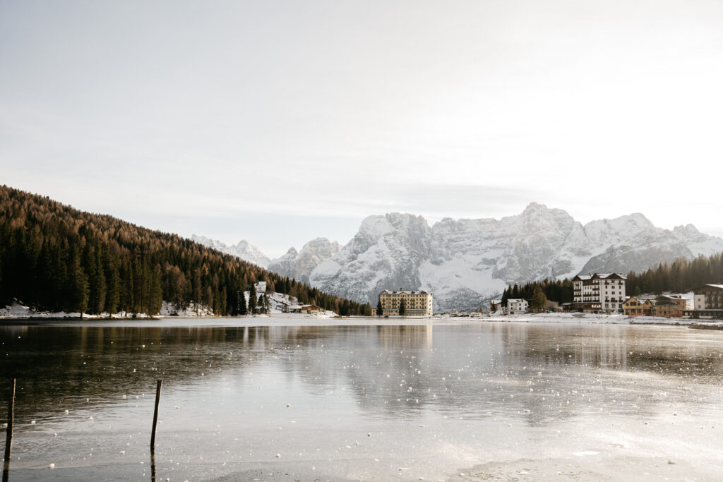 Mountain lake with snowy landscape and buildings.